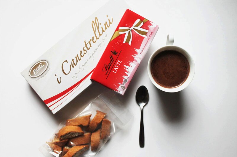 A variety of cozy winter snacks such as Canestrellini, Lindt chocolate, and Cantucci with a cup of Italian hot chocolate